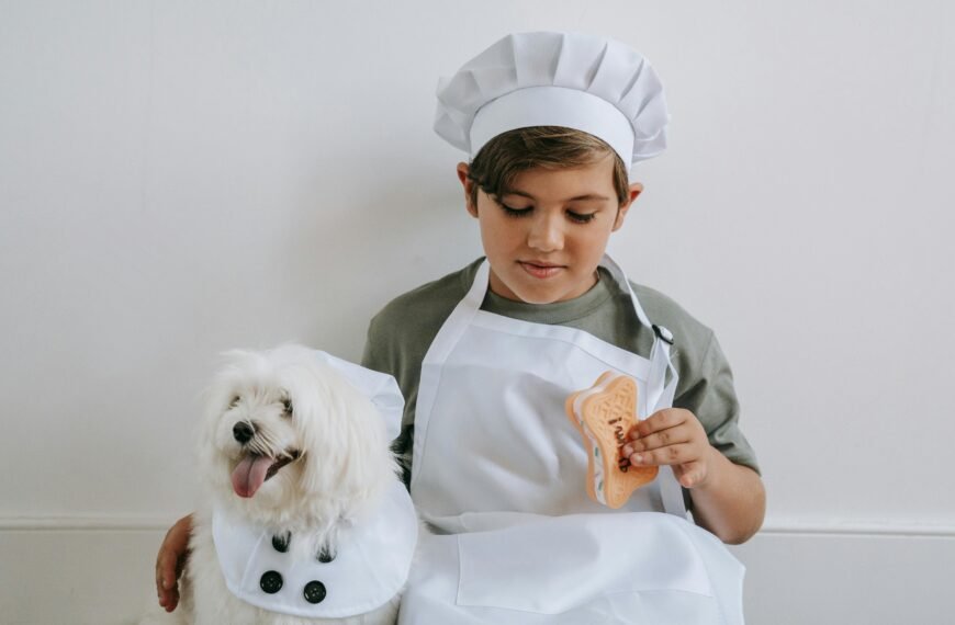 A child dressed as a chef with a dog, both wearing matching outfits, sitting indoors.